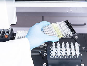 a gloved hand placing labware on the deck of a Felix liquid handler for setting up a Jess automated western blot run