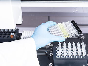 a gloved hand placing labware on the deck of a Felix liquid handler for setting up a Jess automated western blot run
