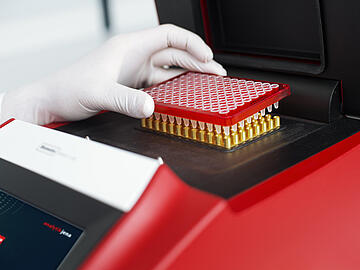 a gloved hand placing a 96-well PCR plate into a Biometra TAdvanced thermal cycler